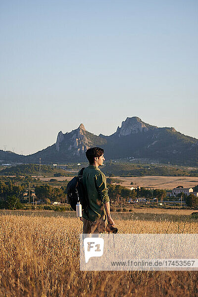 Photographer with a backpack holds a camera in a meadow at sunset