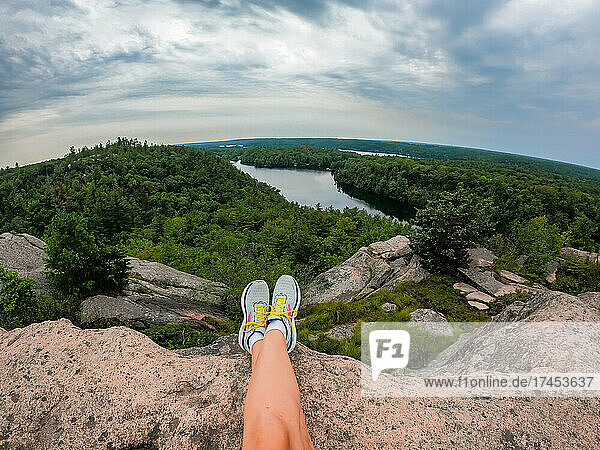 Legs of woman sitting at summit of a hike overlooking lake and trees.