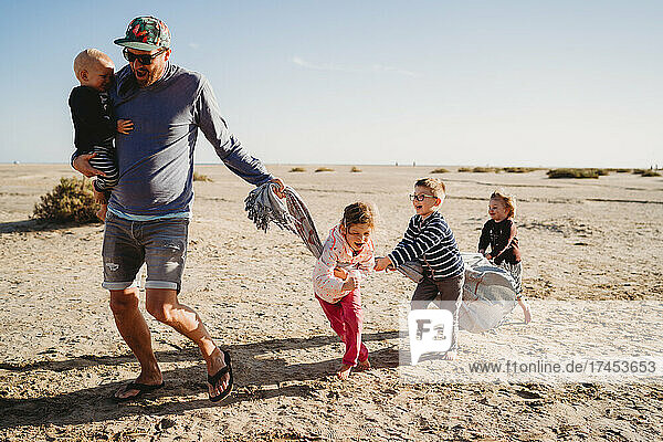 Father and happy children playing with towel at beach on chilly day