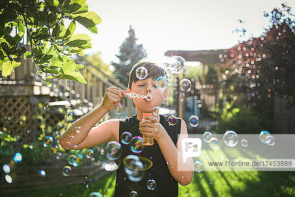 Young boy blowing bubbles in a backyard on a sunny day.