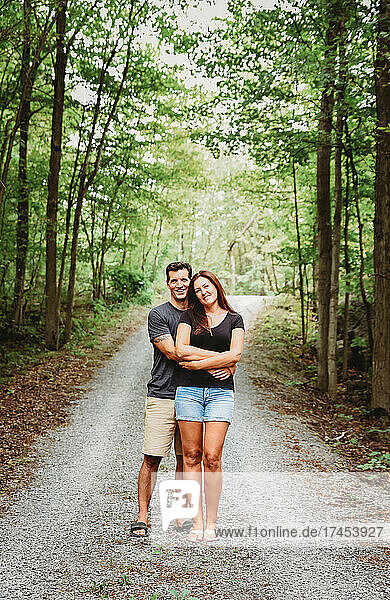 Happy couple embracing on a trail through the woods in summer.