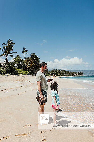 Father and daughter stand on an Oahu beach watching the waves