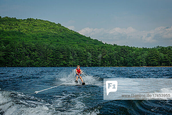 Tween Boy waterskiing on lake with green mountain in distance