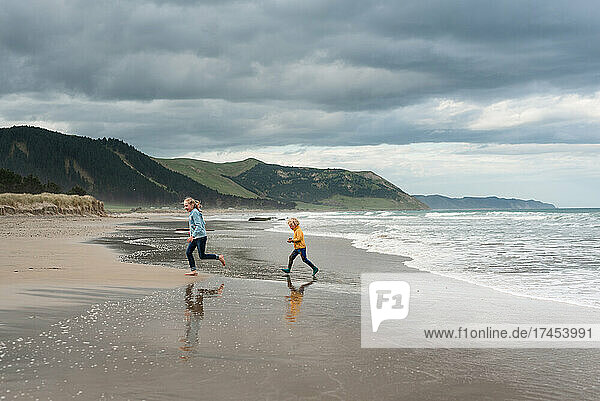 Two children running on beautiful beach on cloudy day in New Zealand