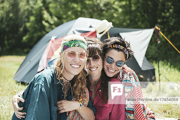 Queer smiling non-binary friends hugging and camping in sun in Poland