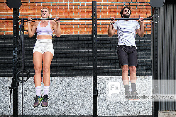 Young man and woman doing pull ups at a crossfit pull up bar