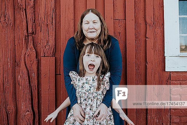 Grandma tickling happy grand daughter in front of red barn