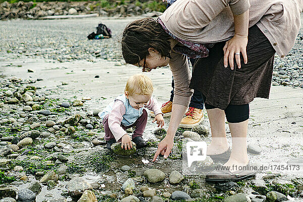 Closeup portrait of a mother and daughter looking under beach rocks