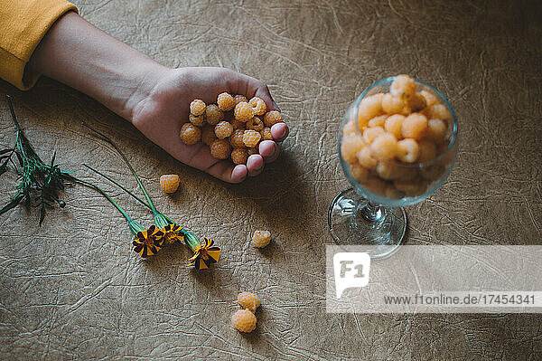 Yellow raspberries in glass and in hand  marigolds on table