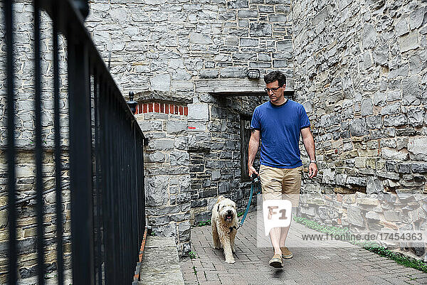 Caucasian man walking fluffy dog through stone alleyway.