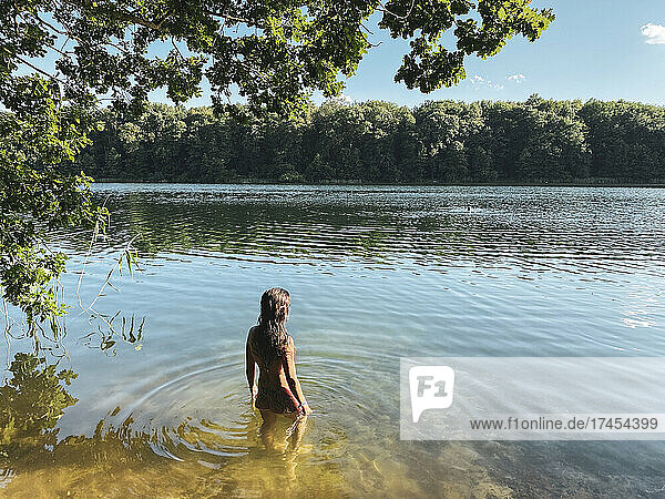 woman stands in beautiful green sandy lake water nude in the forrest