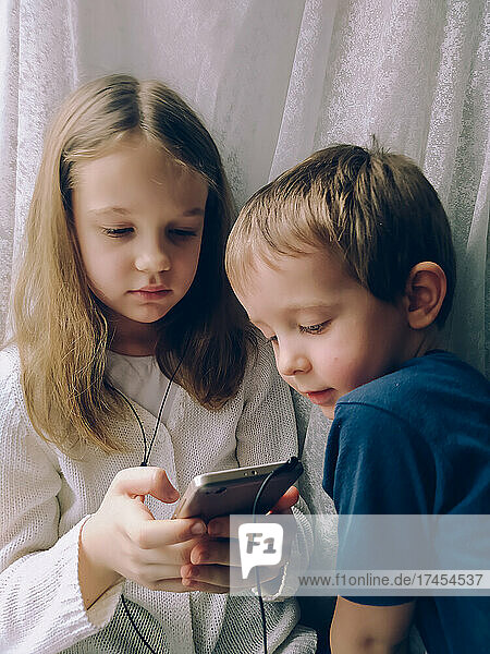Little boy and girl at home with phone and headphones at home