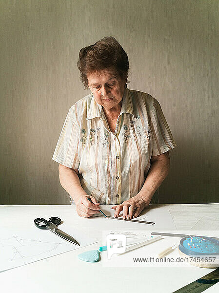 Elderly woman builds medical mask pattern on paper