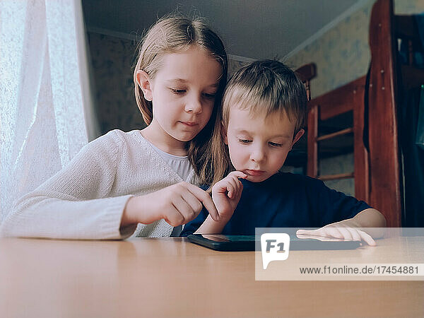Two little kids with gadget tablet at home at the table
