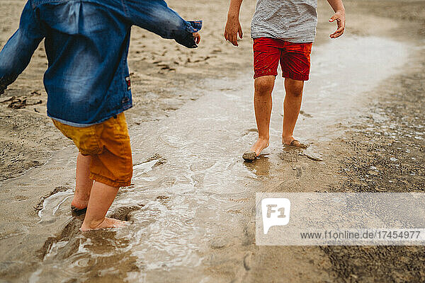 Young children putting feet under wet sand at beach