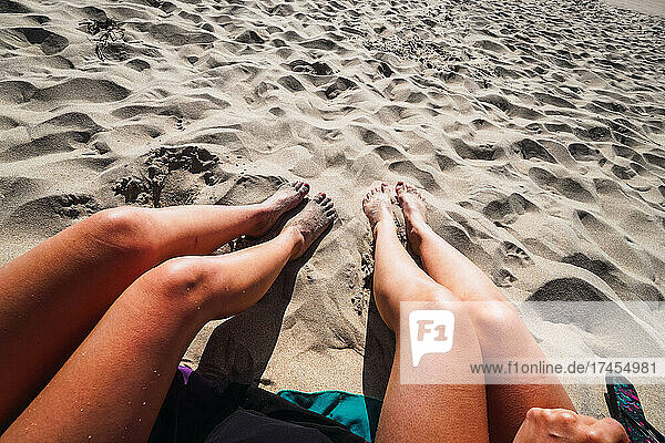 two pair of women's legs in the sand on the beach