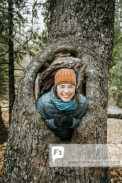 woman wearing hat smiles and laughs inside a large tree knot