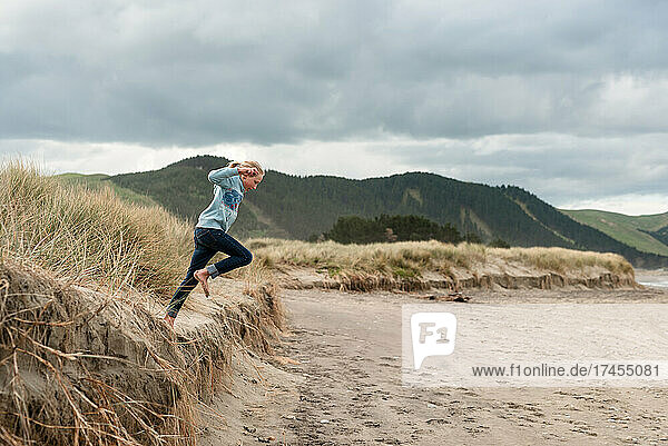 Girl leaping from sand dune at beach in New Zealand