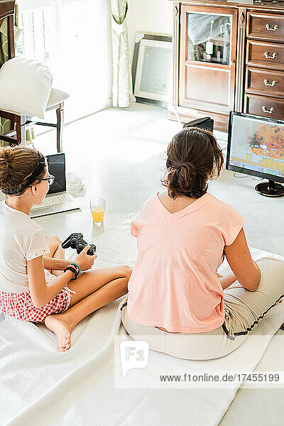 Mother and daughter with gamepads playing video games together at home