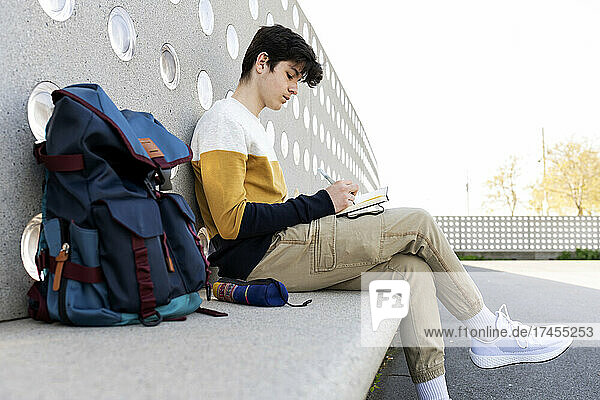 Young male writing notes in a notebook sitting on a bench