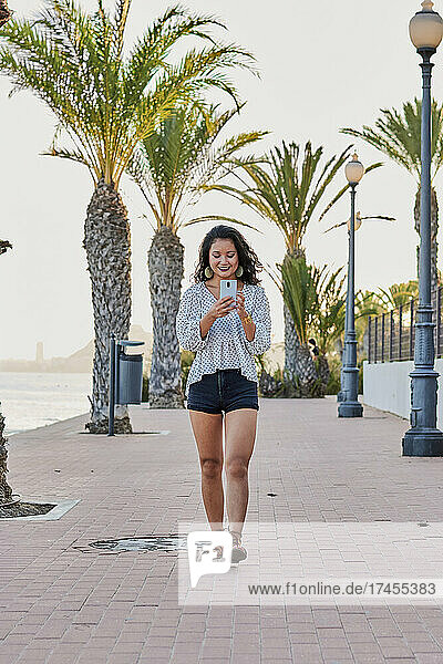 Young Asian woman walks holding her phone in a seaside city