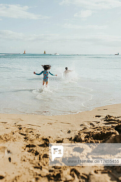Father and daughter run into ocean on beach in Waikiki
