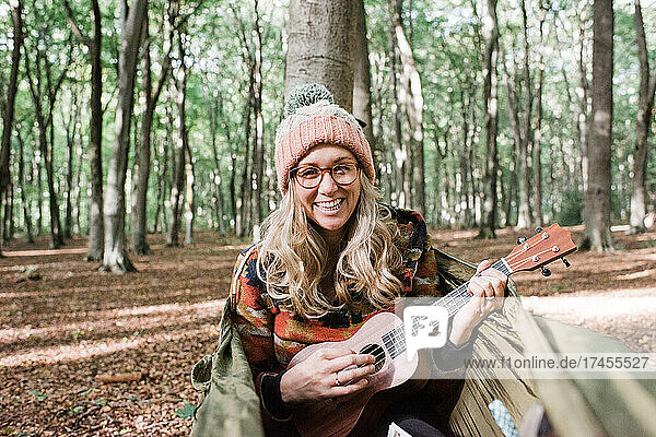 woman laughing whilst playing the ukulele on a hammock in the forest