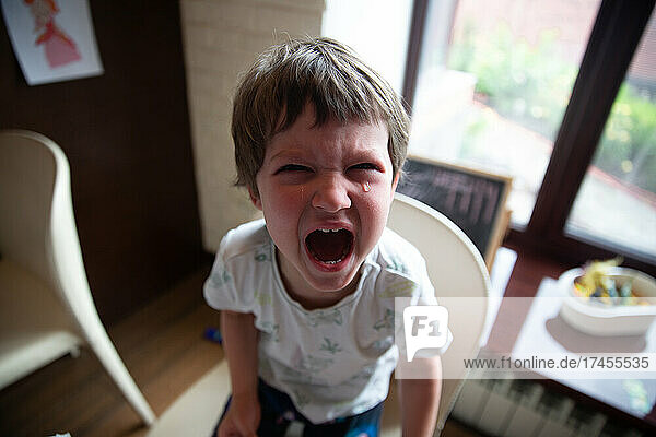 High angle view of a boy crying sitting on a chair at home
