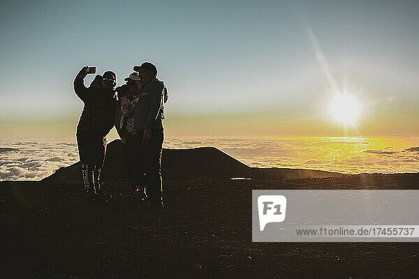 Friends take selfie at sunset on top of Mauna Kea