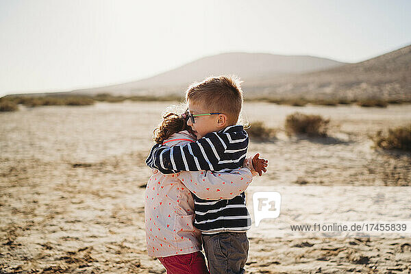 Happy brother and sister hugging at beach during sunset