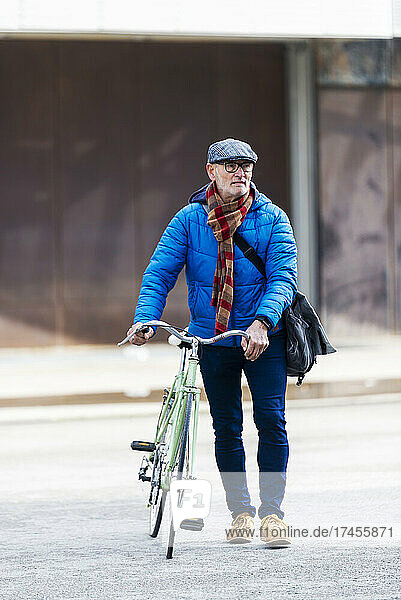 Senior man wheeling bicycle on city street holding a handbag
