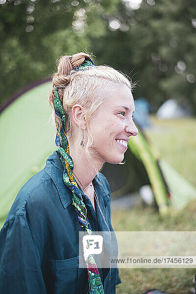 Smiling portrait of blond bohemian woman with ribbon in hair camping