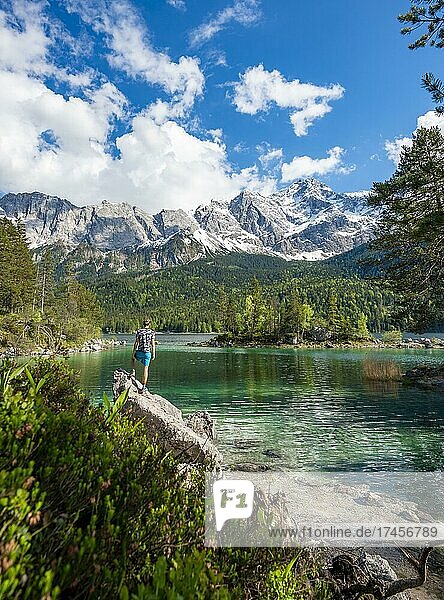 Young man standing on a rock  view into the distance  Eibsee lake and Zugspitze in spring with snow  Wetterstein Mountains  near Grainau  Upper Bavaria  Bavaria  Germany  Europe