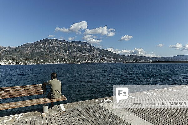 Mann sitzt auf einer Bank am Pier  Bucht von Kalamata  Blick auf Taygetos-Gebirge  Halbinsel Mani  Messenischer Golf  Messenien  Peloponnes  Griechenland  Europa