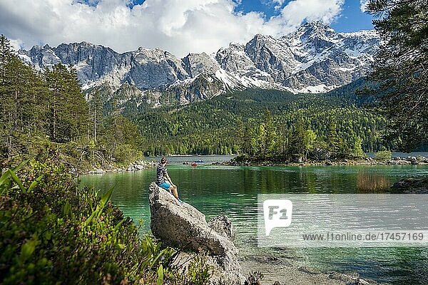 Young man sitting on a rock  view into the distance  Eibsee lake and Zugspitze in spring with snow  Wetterstein Mountains  near Grainau  Upper Bavaria  Bavaria  Germany  Europe
