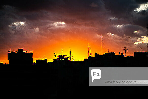 Silhouetted buildings against cloudy sky at sunset