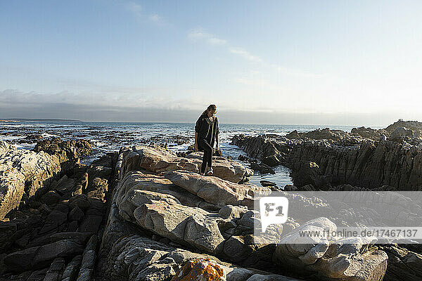 Teenage girl walking across jagged rocks  exploring rock pools by the ocean
