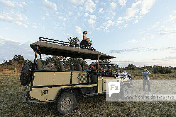 Gruppe von Menschen um Safarifahrzeuge auf einer Pirschfahrt bei Sonnenaufgang