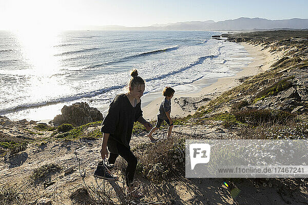 Ein Mädchen im Teenageralter und ihr Bruder rennen einen Weg hinunter zu einem Sandstrand