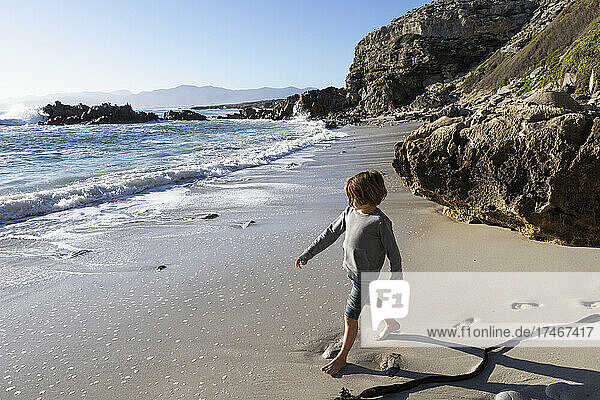 A young boy alone on a small stretch of sand under the cliffs by the ocean.