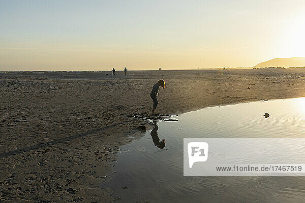 Boy on a beach  looking at his reflection in a water pool  low tide  sunset.