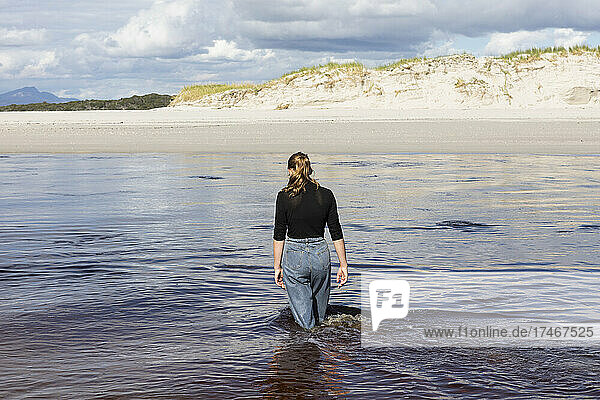A teenage girl wading through a water channel on a wide sandy beach.