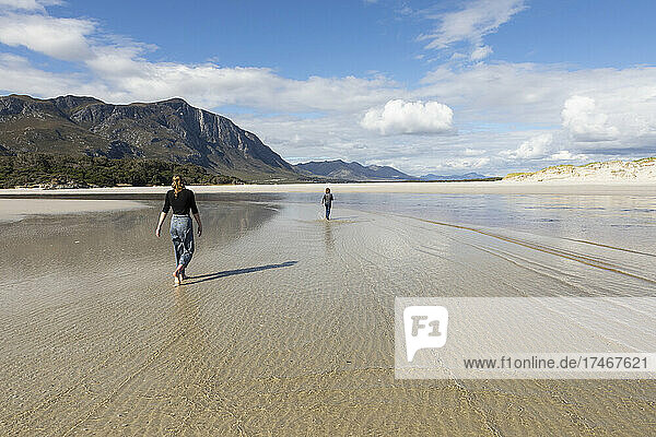 Teenage girl and her younger brother walking across a wide beach