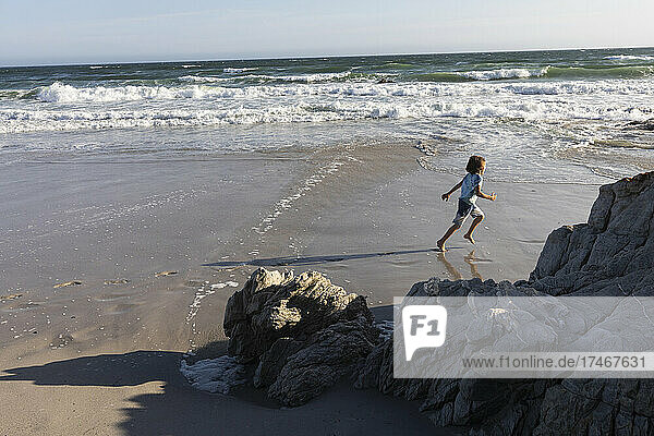 Ein Junge  der am Ufer eines Sandstrandes durch den Sand läuft.