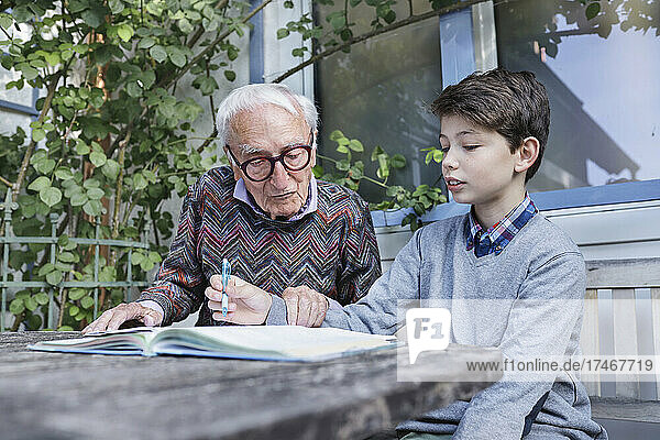 Grandfather assisting boy studying in backyard