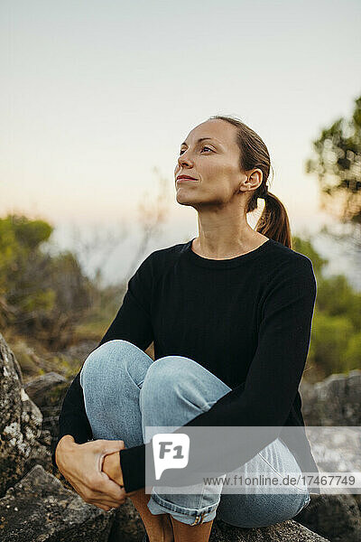 Woman contemplating while hugging knees on rock