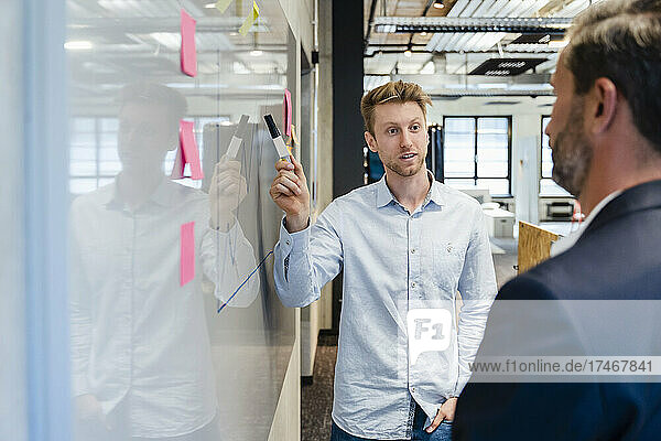 Young businessman with pen explaining colleague over graph at whiteboard