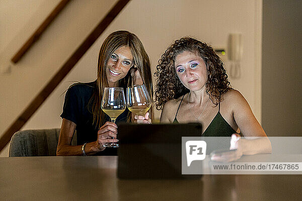 Mature female friends with wineglasses using laptop at table