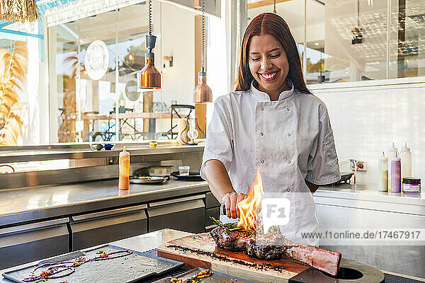 Smiling female chef smoking steak in kitchen