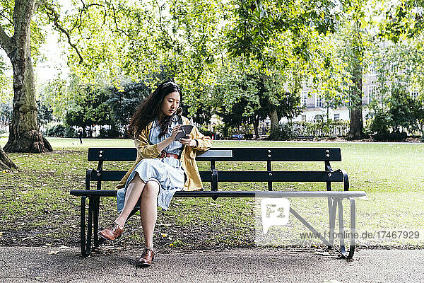 Frau liest Tagebuch  während sie auf Bank im Park sitzt
